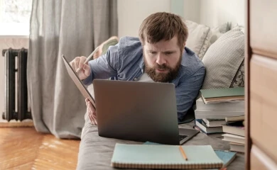 An adult studies his laptop with a tablet in their hands