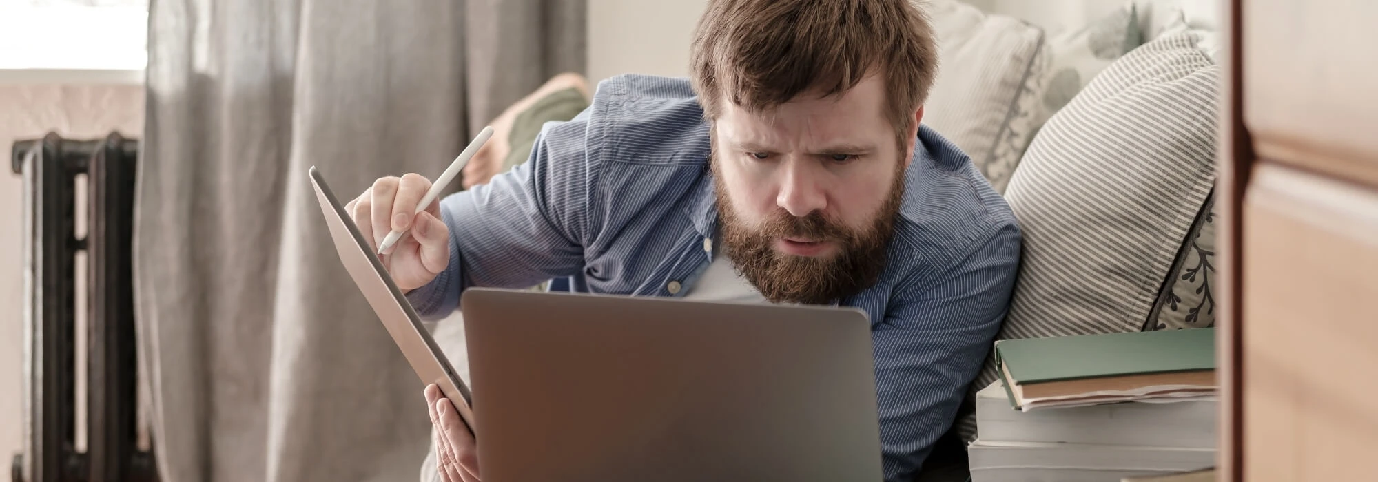 An adult studies his laptop with a tablet in their hands